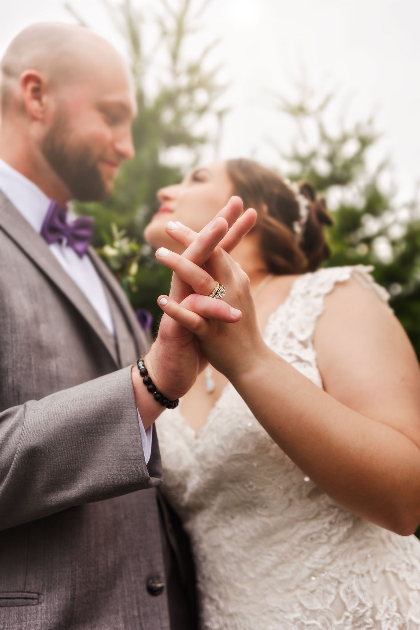 Bride and groom holding hands with wedding rings visible, sharing an intimate moment outdoors in Allentown, Pennsylvania, with soft focus on their faces and greenery in the background.